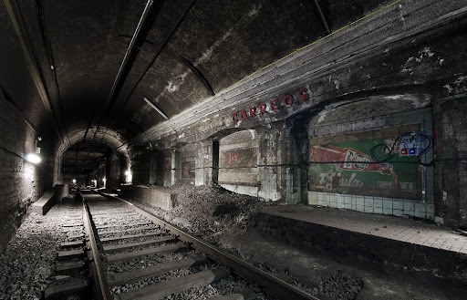 Abandoned metro tunnel at the former Correos station in Barcelona, featuring derelict platforms and graffiti-covered walls.