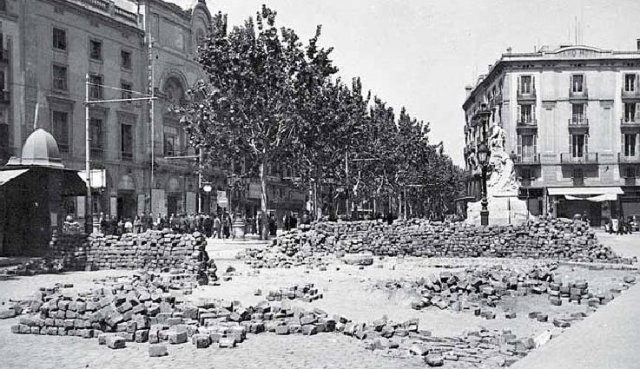 Historical photo of 1930s Barcelona with stone barricades in the street and buildings in the background.