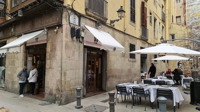 Exterior view of Cal Pep, a popular restaurant in Barcelona, with a traditional stone facade and outdoor seating under white umbrellas.