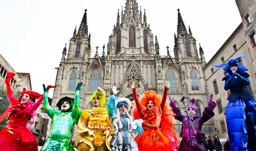 Performers dressed in colorful and elaborate costumes at Barcelona Carnival in front of a cathedral.