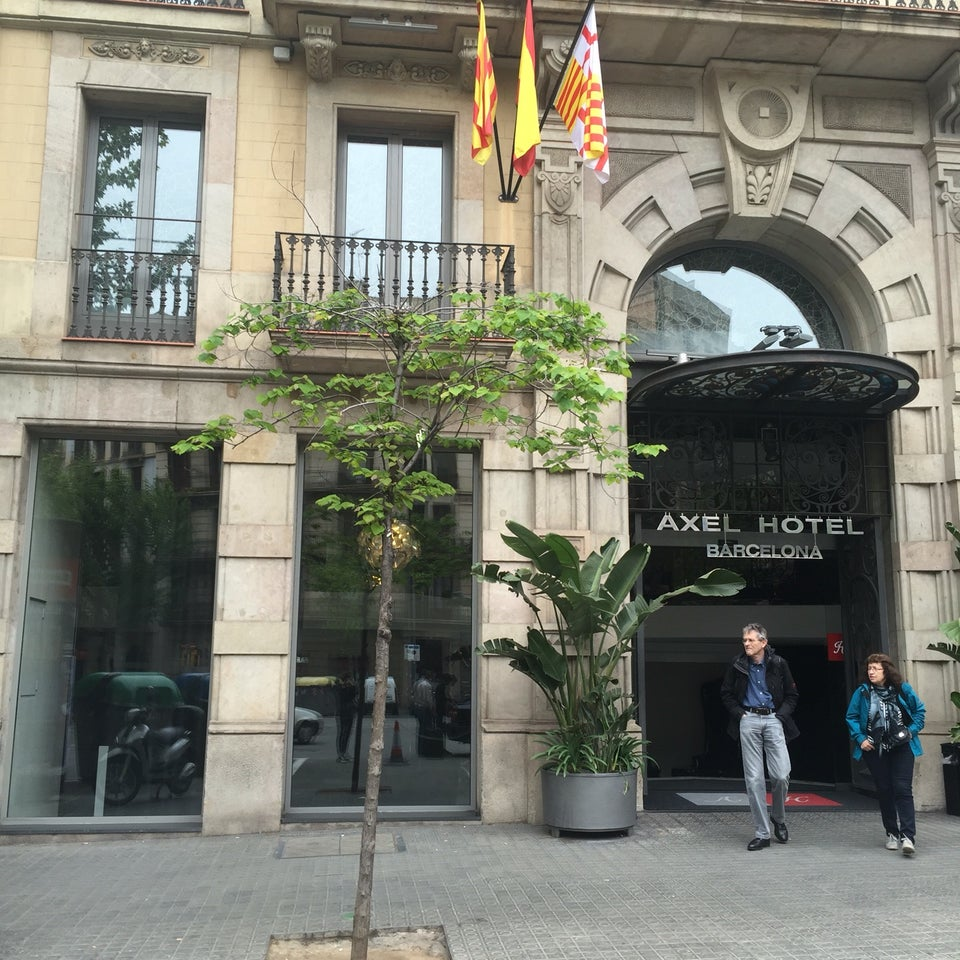 Entrance of Axel Hotel in Barcelona, featuring flags and ornate architectural details.