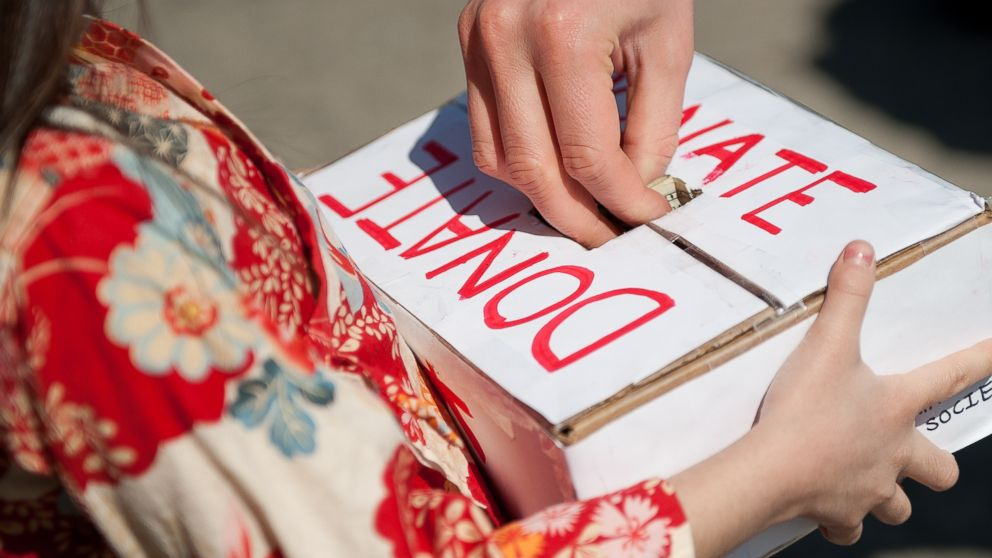 A person placing money into a donation box labeled with "donate" during a fundraising event.