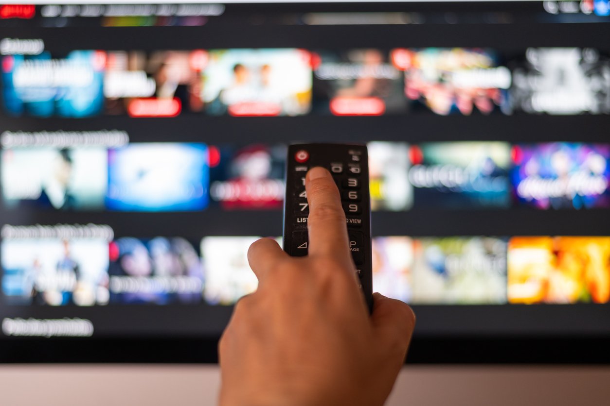 Person using a remote control to browse through a streaming platform's selection of shows and movies.