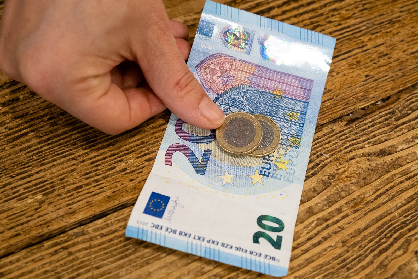 hand putting one 20 euro bill and 2 1 euro coins on a table